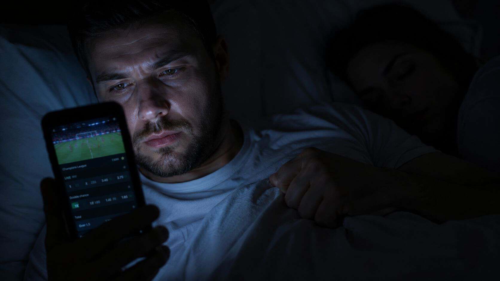 Mężczyzna obstawiający mecze w nocy na telefonie — uzależnienie od hazardu w codziennym życiu